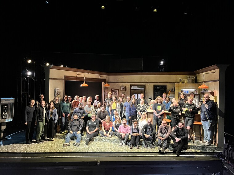 The cast and crew of The Capulets and the Montagues stands smiling on the set of the production.
