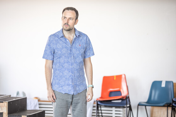 A man in a blue shirt stands in the rehearsal room