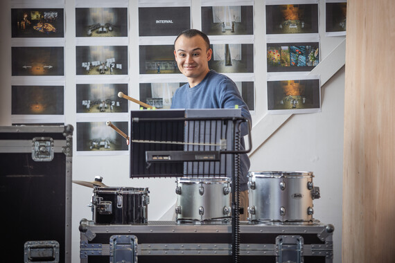A man plays a set of silver drums in the rehearsal room