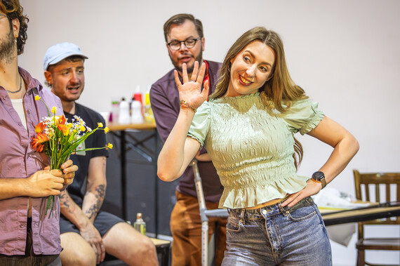 A woman waves and smiles in the rehearsal room