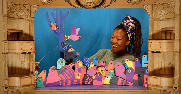 Multicoloured cardboard bird puppets with woman singing in cardboard theatre