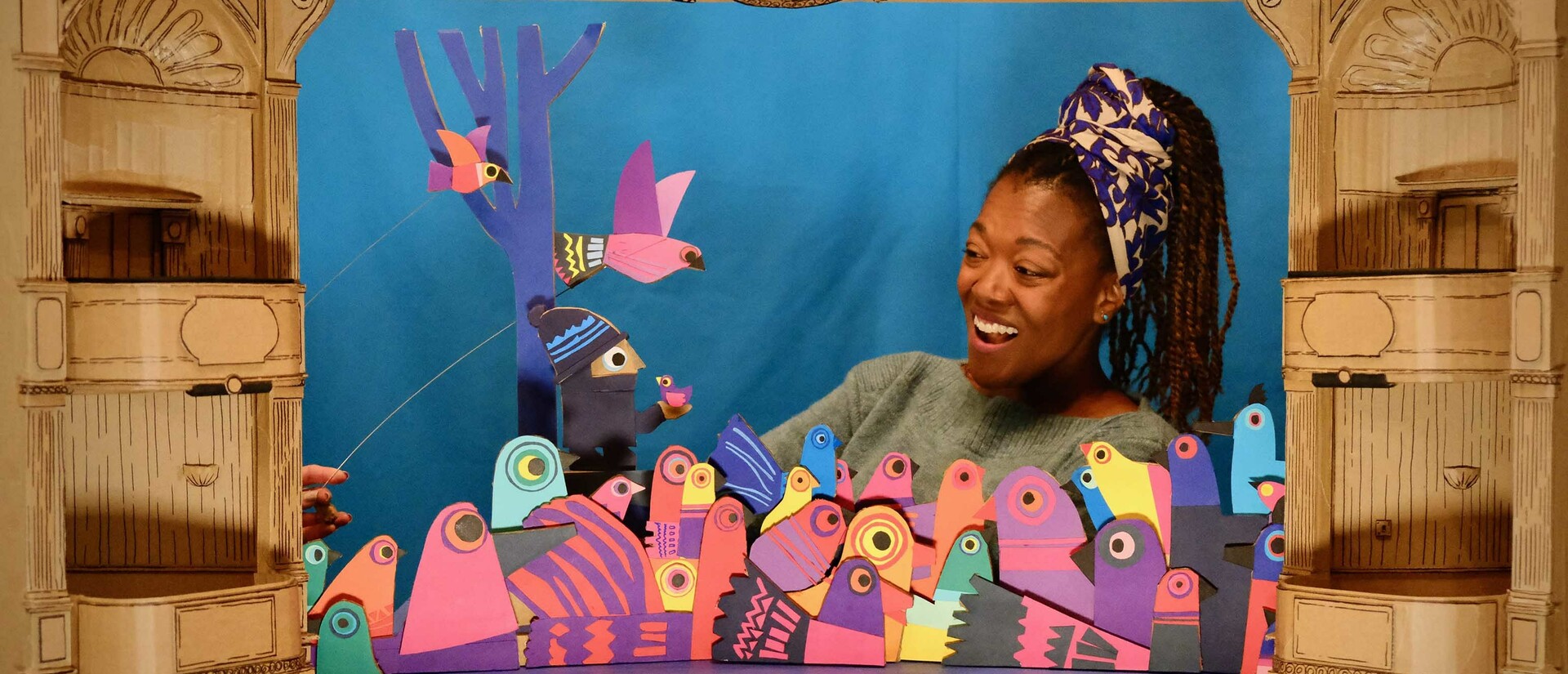 Multicoloured cardboard bird puppets with woman singing in cardboard theatre