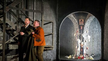 Don Giovanni and Leporello are standing stage right next to a staircase. Leporello is holding his coat and Don Giovanni.