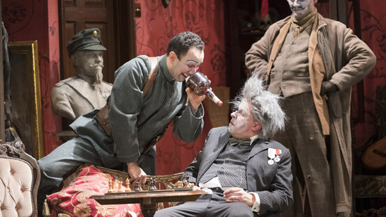 Simone sits in a chair. Rinuccio straddles the side of the chair, leaning towards Simone. Betto stands behind