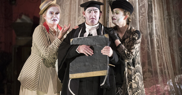 Ser Amantio stands between Nella and La Ciesca. He is clutching a large, black book