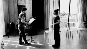 Singer looking at sheet music whilst watched by a director