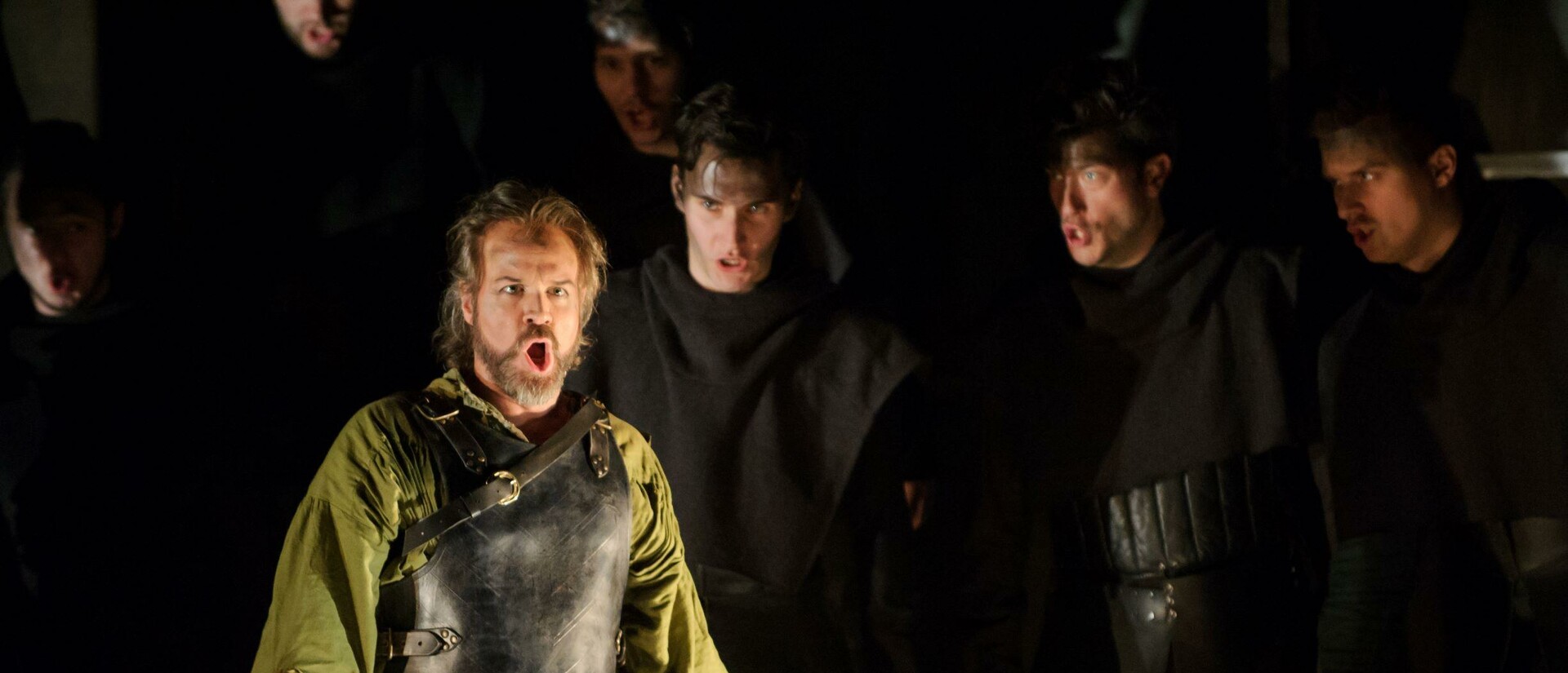 Nello singing in front of chorus of men