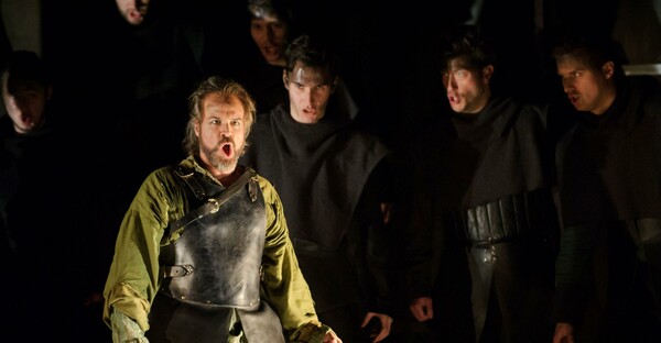 Nello singing in front of chorus of men